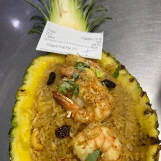 Pineapple boat dessert topped with shrimp and sauce, garnished with raisins and a small label.