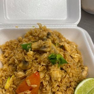 Takeout styrofoam box with fried rice, chicken, vegetables, and a lime wedge