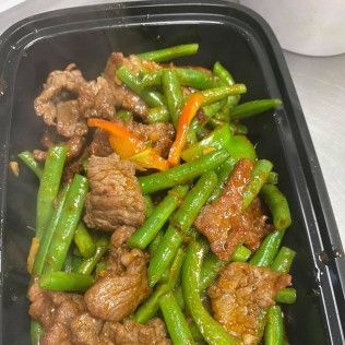 Beef and green beans with sliced peppers in a black takeout container.