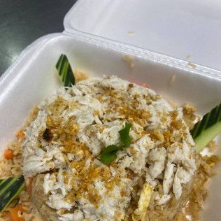 Plastic takeout container with rice topped with shredded chicken and seasoning, garnished with cucumber slices