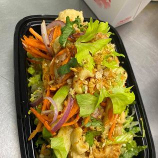 Black tray of salad with lettuce, carrots, red onion, and dressing on a table