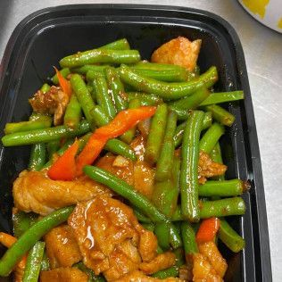 Stir-fried green beans and red peppers with chicken in a black takeout container