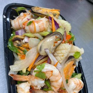 Seafood salad with shrimp, mussels, and vegetables in a black takeout container