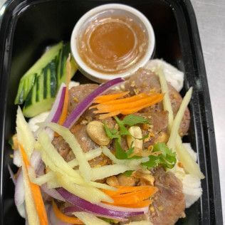 Assorted sliced vegetables and meat in a black takeout container with a small cup of sauce