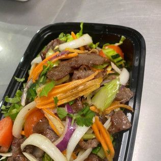 Black takeout container with stir-fried beef and colorful vegetables, including carrots, onions, peppers, and cilantro.