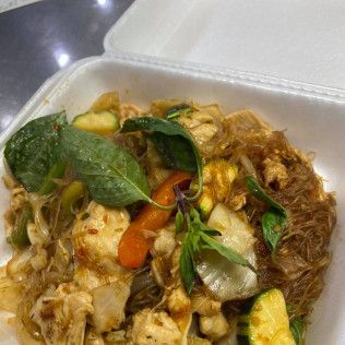 Takeout container with stir-fried noodles, greens, and vegetables in brown sauce