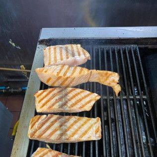 Four striped fish fillets grilling on a barbecue, with orange-brown grill marks.