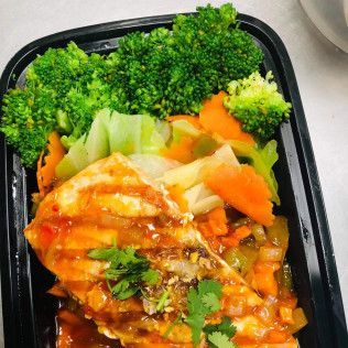 Black takeout container with sauced chicken, broccoli, and vegetables