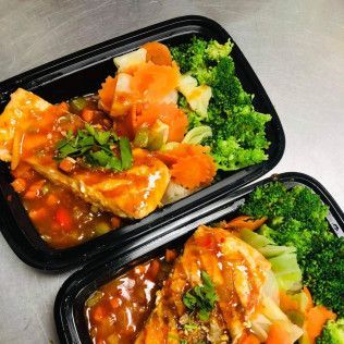 Two takeout trays of saucy chicken with broccoli and carrots on rice