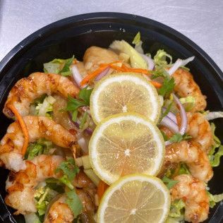 Shrimp salad bowl topped with lemon slices, greens, and shredded vegetables
