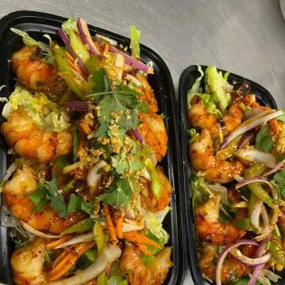 Two black takeout containers of saucy stir-fried shrimp with onions, peppers, and cilantro