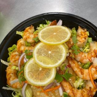 Shrimp salad topped with lemon slices, red onion, and greens in a black bowl