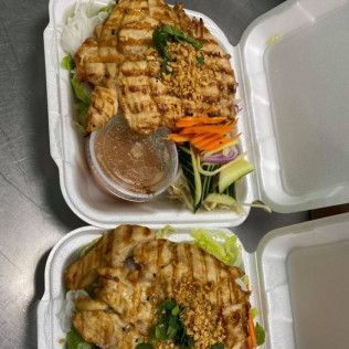 Two takeaway boxes with grilled chicken, rice, salad, and dipping sauce on a table