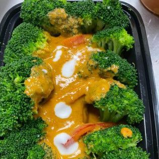 Broccoli and saucy orange curry in a black takeout tray with white drizzle