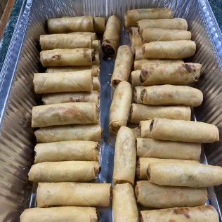Tray of golden-brown spring rolls arranged in rows in an aluminum pan