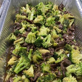 Steamed broccoli and beef in a foil tray, topped with green sauce.