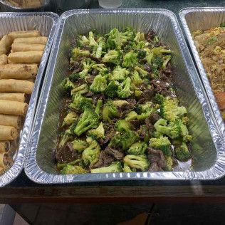 Buffet trays with spring rolls, broccoli and beef, and a rice dish on a table