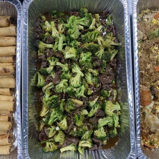 Aluminum tray of roasted broccoli and dark mushrooms, with other side dishes partially visible beside it