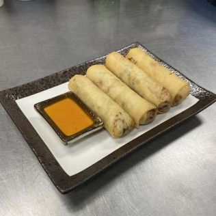 Plated spring rolls with orange dipping sauce on a rectangular dish