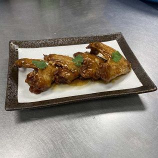 Glazed chicken wings garnished with green herbs on a rectangular white plate