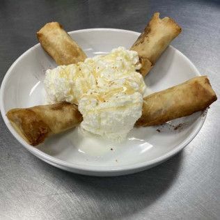 Plate with four fried spring rolls around a scoop of vanilla ice cream topped with syrup on a stainless steel table