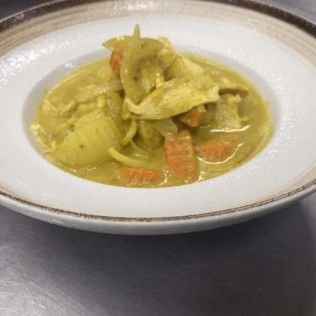 A white bowl of yellow curry soup with vegetables on a gray surface.