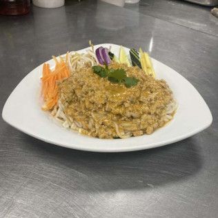 Plate of creamy curry over noodles, garnished with herbs and served with shredded vegetables on a white plate.