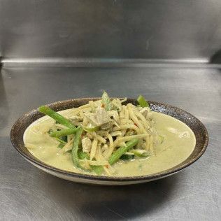 Bowl of creamy green curry with sliced vegetables on a metal countertop