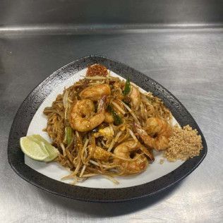 Plate of shrimp pad thai with lime wedge on a black tray in a stainless steel kitchen