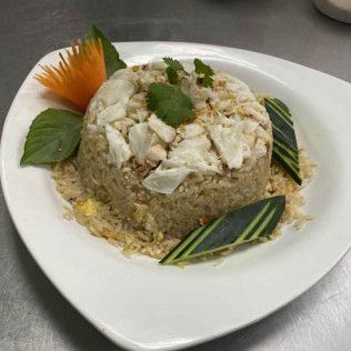 Plate of molded fried rice topped with crab, garnished with herbs and carved vegetables on a white dish