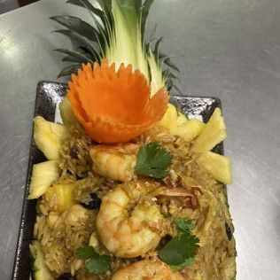 Shrimp fried rice garnished with pineapple wedges, cilantro, and a carved carrot flower in a black bowl