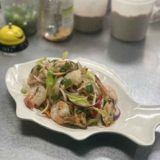 Salad with sliced vegetables and herbs on a white serving plate on a metal countertop