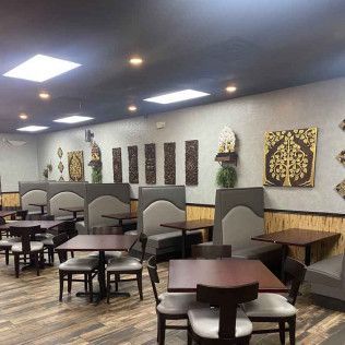 Empty restaurant dining area with dark tables and booths, warm lighting, and decorative wall art.