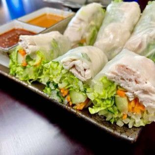 Fresh vegetable spring rolls on a dark plate with dipping sauces in the background