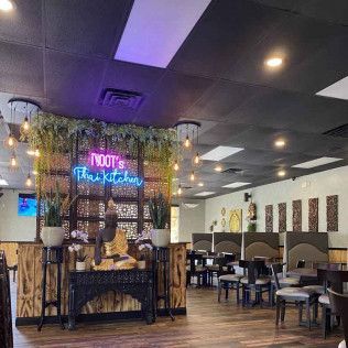 Dimly lit restaurant interior with neon sign, hanging plants, and empty tables and chairs