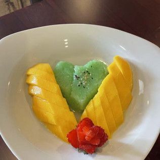 Sliced mango and kiwi arranged as a heart with strawberries in a white bowl