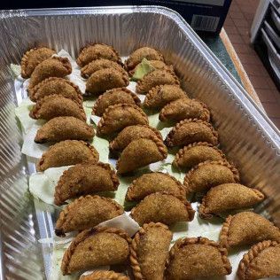 Tray of golden-brown fried turnovers on a white paper-lined aluminum pan.