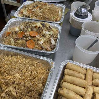Tray of assorted takeout dishes on a table, including spring rolls, fried rice, and mixed vegetables with sauce.
