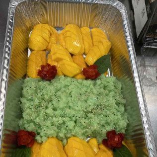 Aluminum tray of yellow mango slices over green rice, garnished with red flowers and a mint leaf