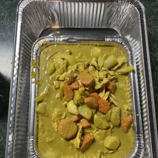 Foil tray of green curry pasta with chunks of vegetables and sauce