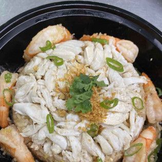 Shrimp and shredded crab in a black bowl, topped with green onions, herbs, and seasoning