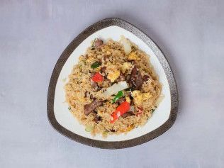 Triangular white plate of fried rice with mixed vegetables on a light surface