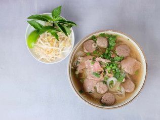 Two bowls of noodle soup with herbs, sliced meat, and bean sprouts on a light gray surface