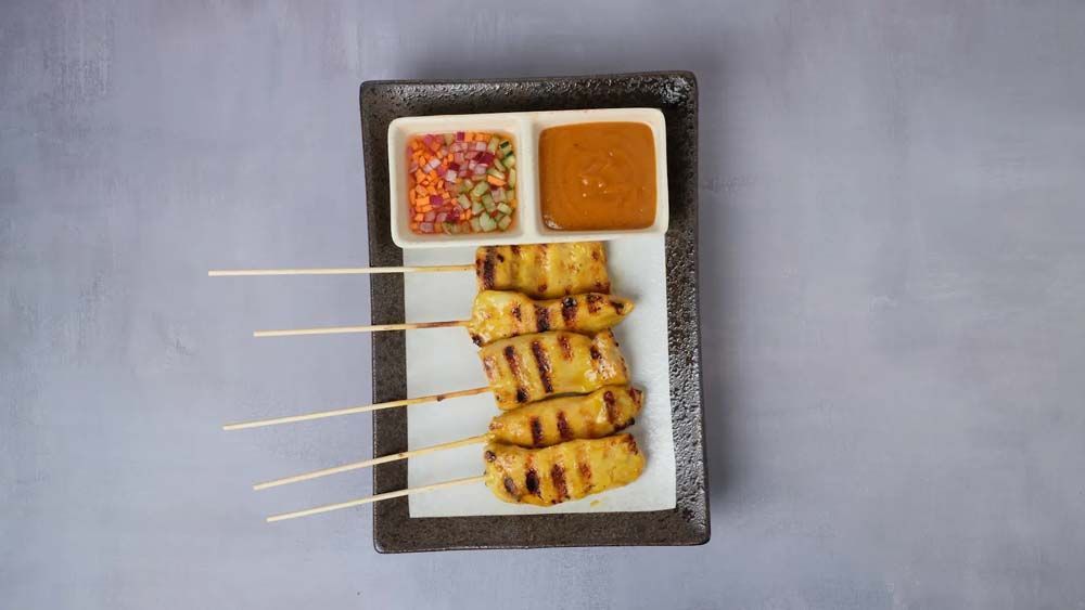 Grilled skewered chicken with dipping sauces on a rectangular platter