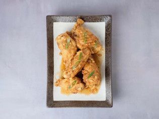 Plate of crispy fried chicken wings on a rectangular white dish with sauce drizzle