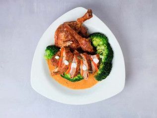 Plated roasted chicken with broccoli and orange sauce on a white dish