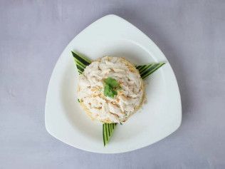 Scoop of creamy salad on a white triangular plate, garnished with green herbs and leaves