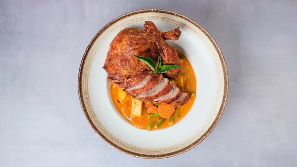 Roasted meat with sliced garnish on a white plate, drizzled with orange sauce and herbs
