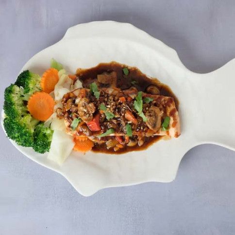Fish-shaped white plate with saucy meat and vegetables, garnished with broccoli and carrot slices