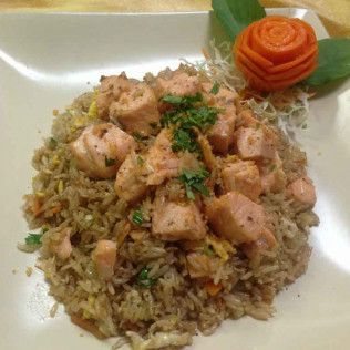 Fried rice topped with diced chicken and herbs on a white plate, with a carrot garnish.